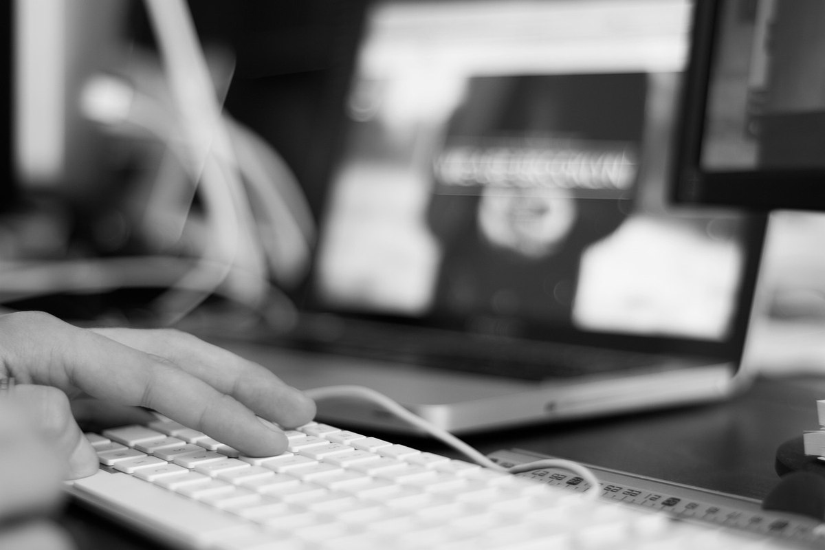 Main tapant sur un clavier d'ordinateur, avec un portable et écrans flous en arrière-plan dans un environnement de travail Main tapant sur un clavier d'ordinateur, avec un portable et écrans flous en arrière-plan dans un environnement de travail