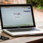 Laptop affichant la page Google sur table en bois extérieure avec téléphone