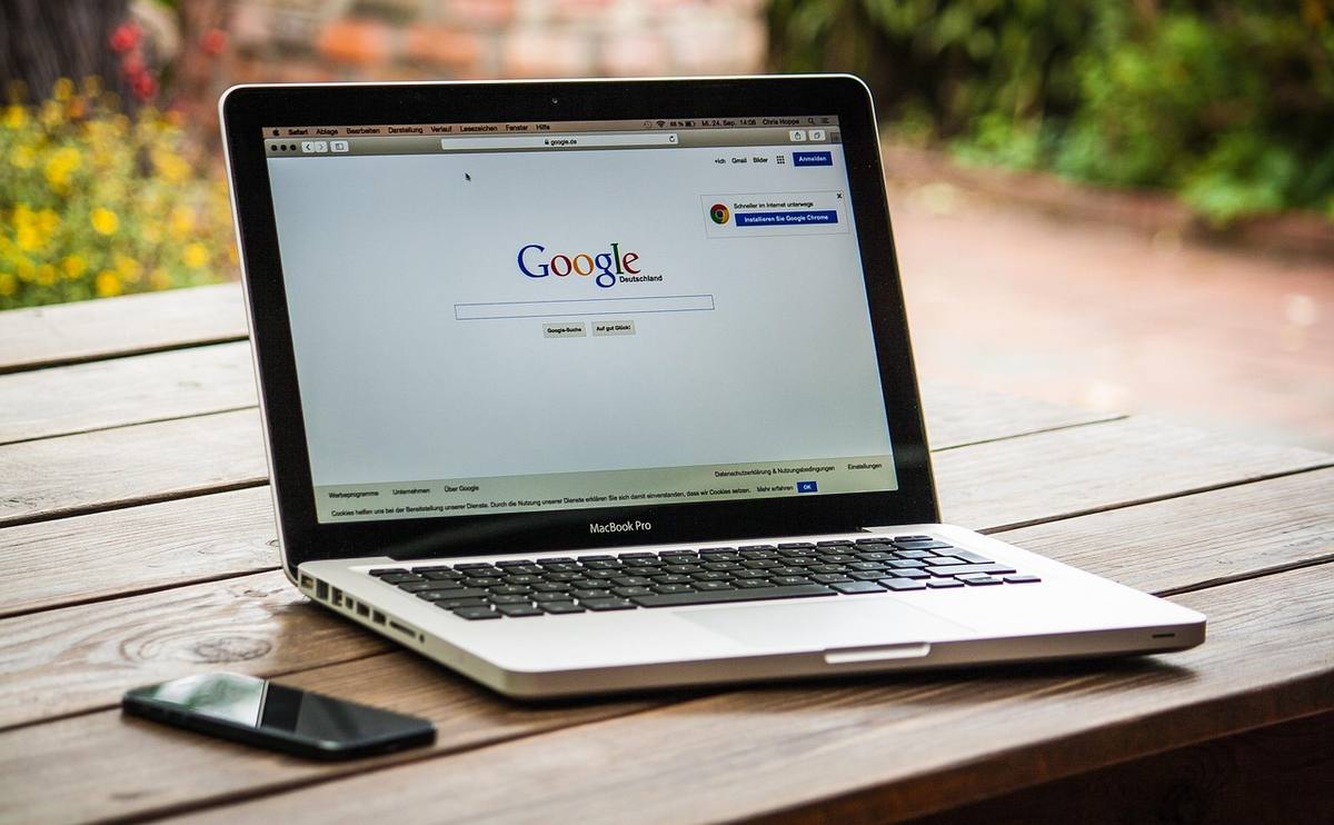 Laptop affichant la page Google sur table en bois extérieure avec téléphone