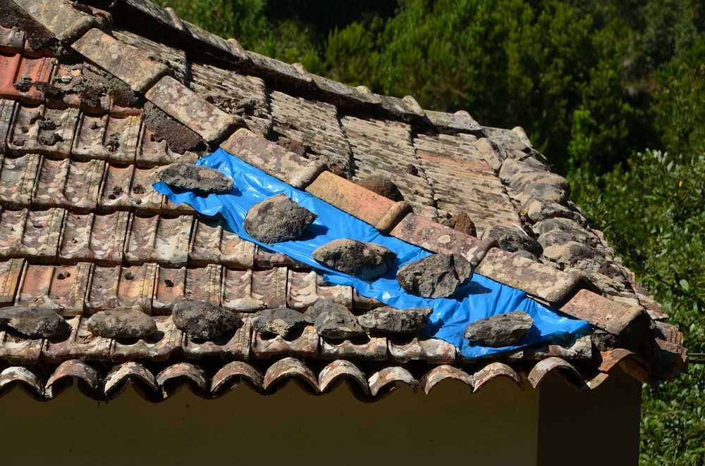 ALT: Des pierres maintenues par une bâche bleue sur une toiture en tuiles