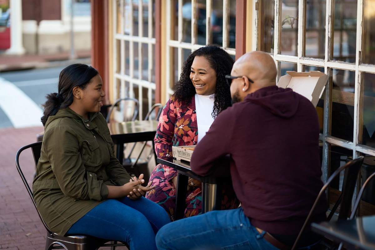 Trois individus en conversation autour d'une table de terrasse dans un café urbain Trois individus en conversation autour d'une table de terrasse dans un café urbain